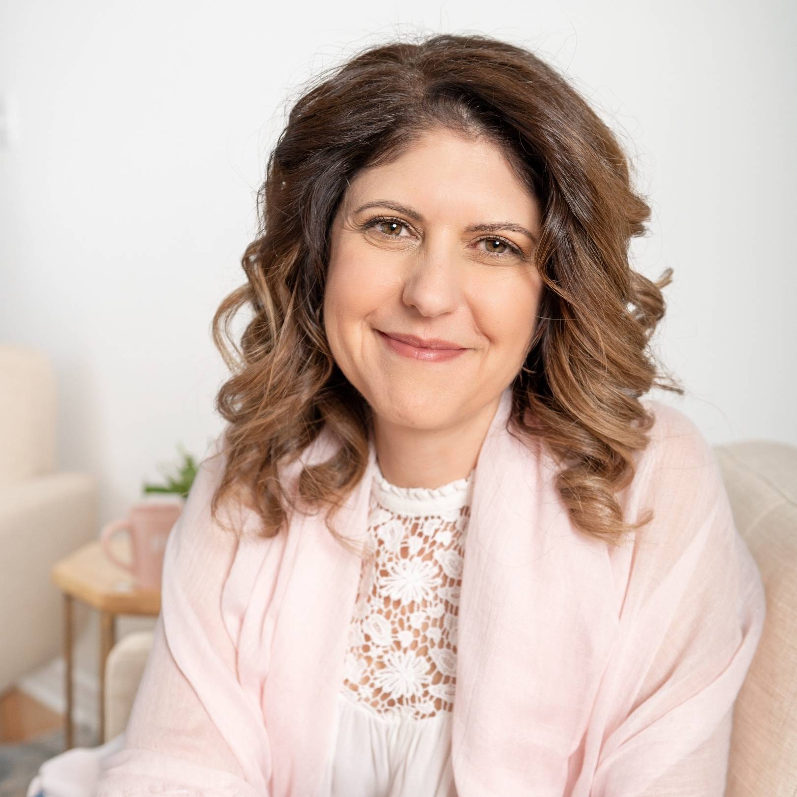 Marie Mota-Lee headshot. Closed mouth smile. Shoulder length brown curled hair.